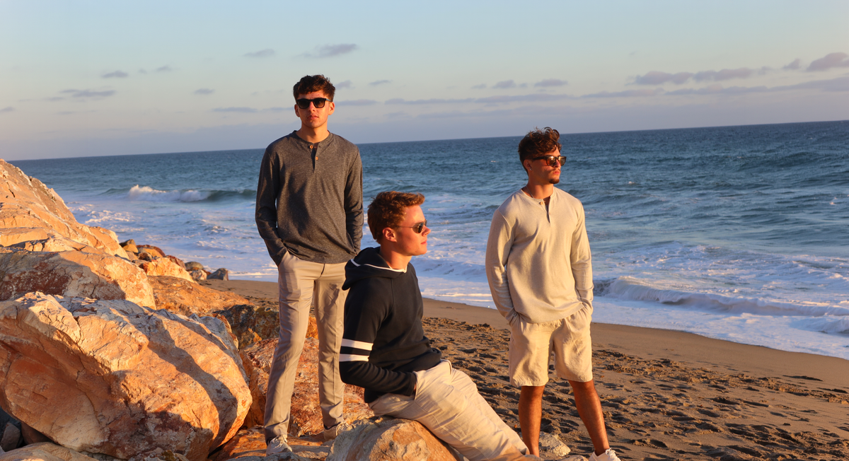 Friends on the rocks at a sunset beach in Ladd & Co Herringbone Henleys and a navy pullover hoodie